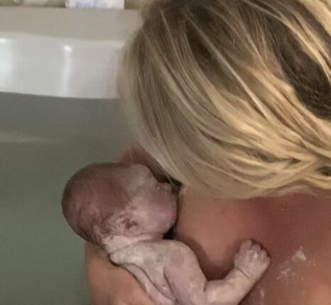 Mother holds vernix covered newborn in birth tub