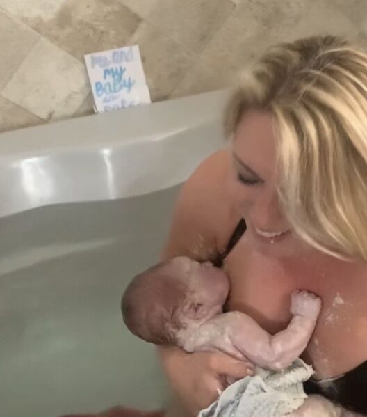 Mother smiles holding baby in birth tub